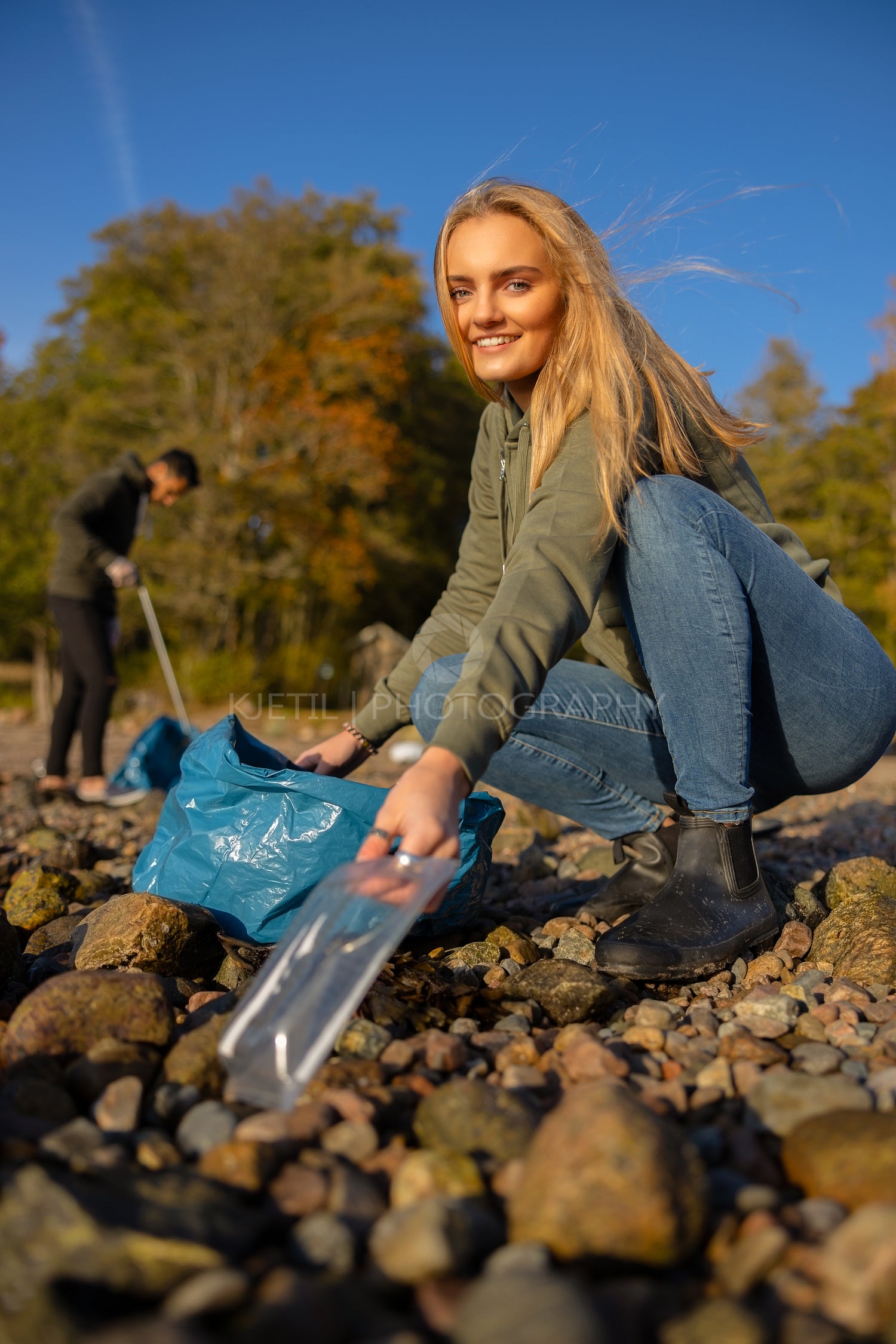 Smiling young woman picking up plastic at rocky beach