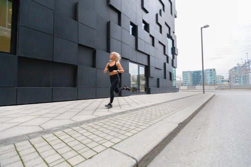 Focused fast running woman wearing sports top in modern city environment