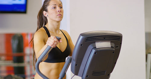 Focused woman training on ellipse exercise machine in fitness gym