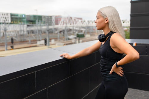 Fit Female Athlete with Headphones and Smartwatch Rests After Workout On Bridge