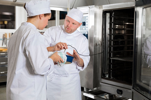 Chef helps student with cooking in a large kitchen