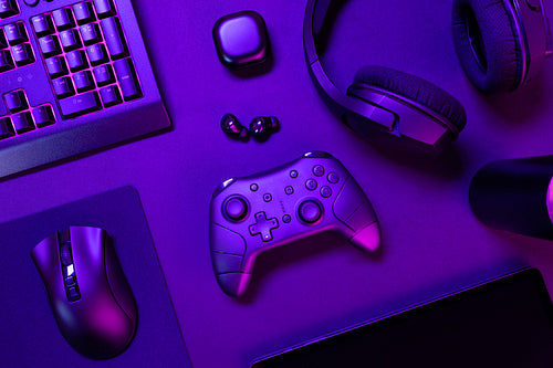 Top view of purple lit keyboard amidst various modern gaming devices