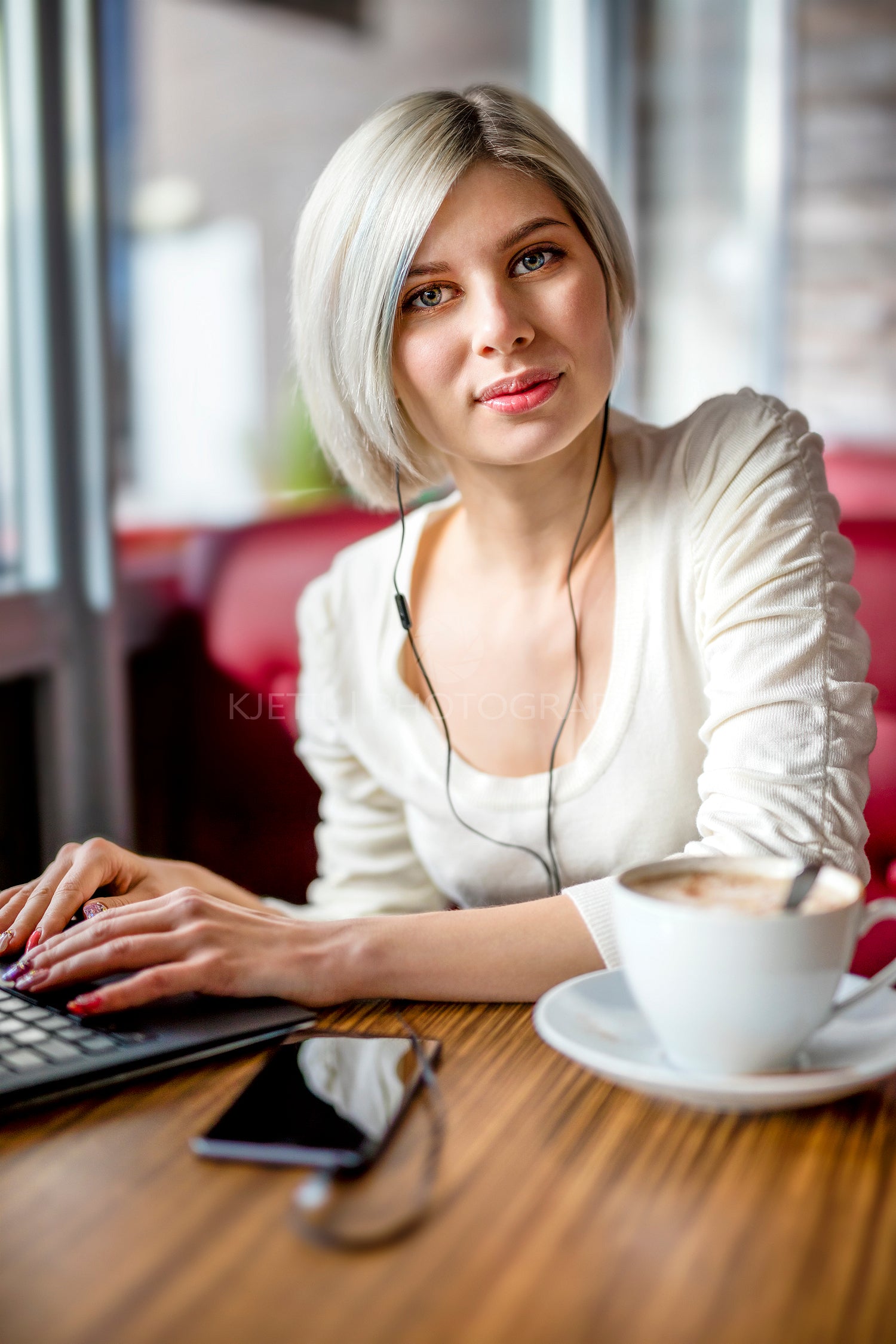 Young Woman Listening Music While Working On Laptop In Cafe