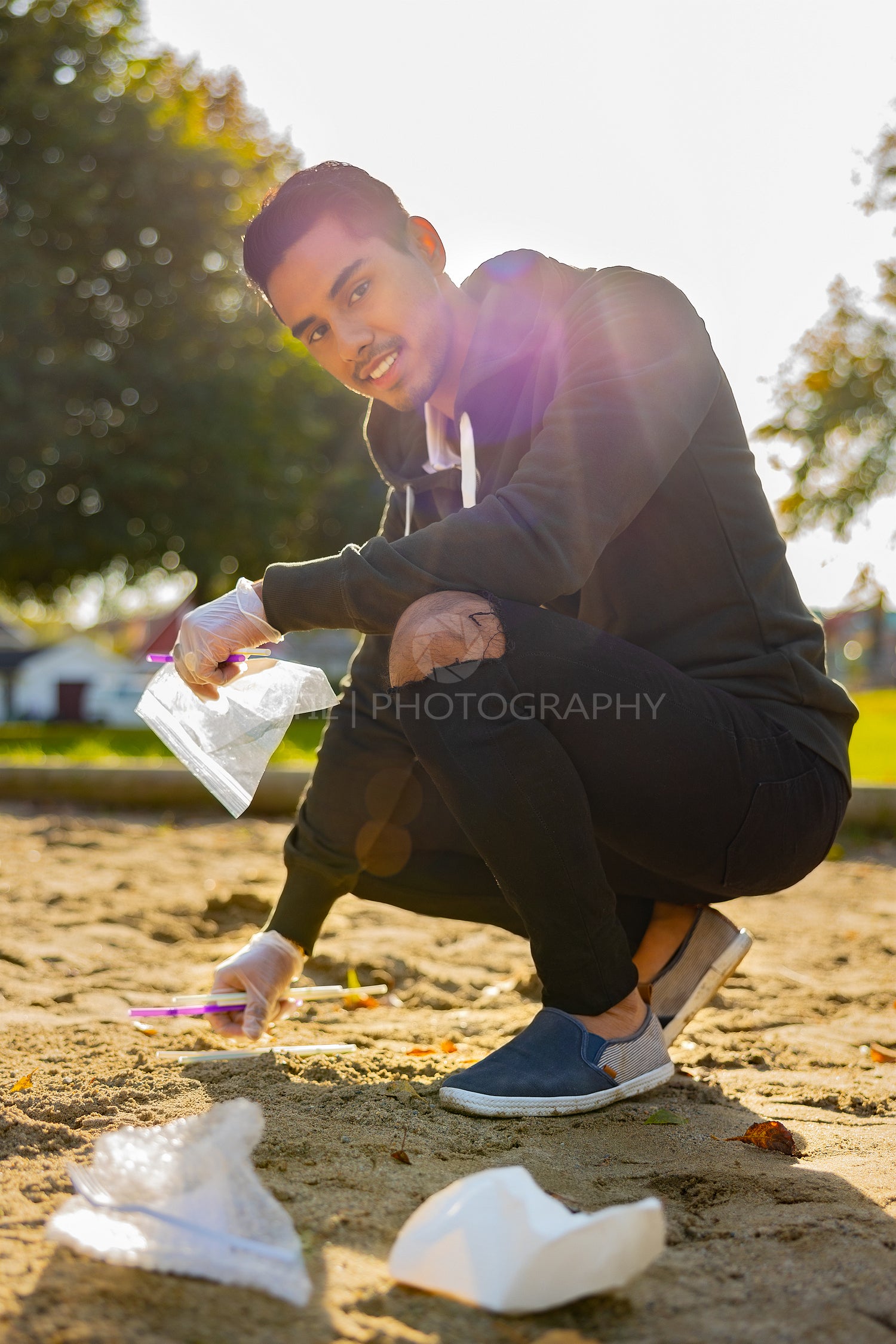 Back lit of smiling man cleaning garbage on sand at park