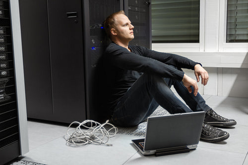 Exhausted Mid Adult Male Technician Against Server Rack At Datacenter