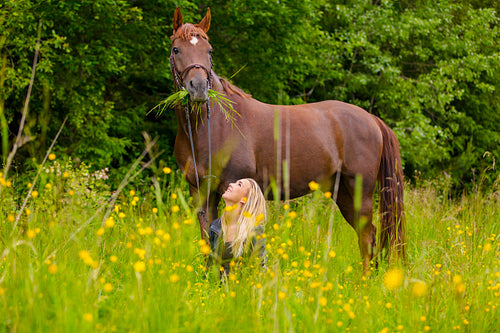 Smiling woman sitting in the meadow and communicate with her arabian horse