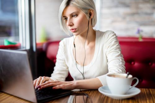 Woman Listening Music While Working On Laptop In Cafe