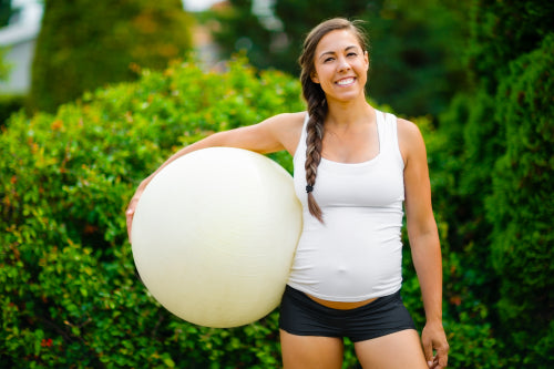 Smiling Young Expectant Mother Holding Exercise Ball In Park