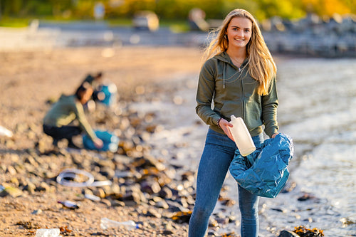 Beautiful Young Volunteer holding bottle and garbage bag at beach