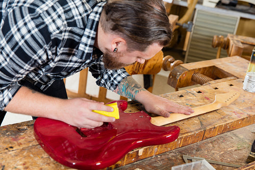 Close-up of craftsman sanding a guitar neck in wood at workshop