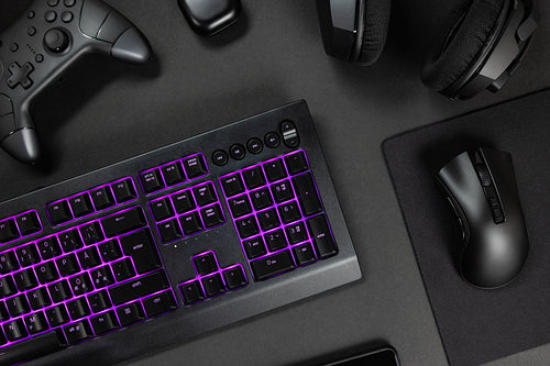 Purple lit keyboard surrounded by various modern wireless gadgets
