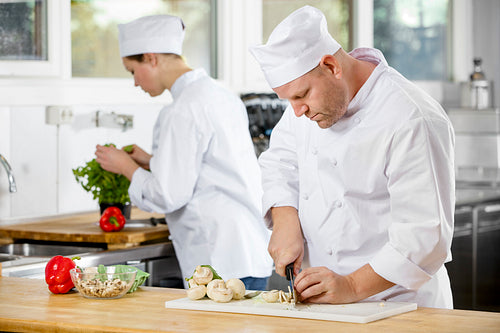 Two professional chefs preparing vegetables in large kitchen