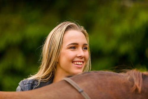 Close-up of smiling woman patting her arabian horse with grass in the field