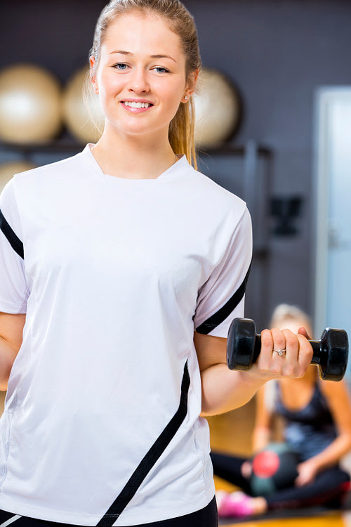 Smiling woman in workout outfit holds dumbbell at fitness gym