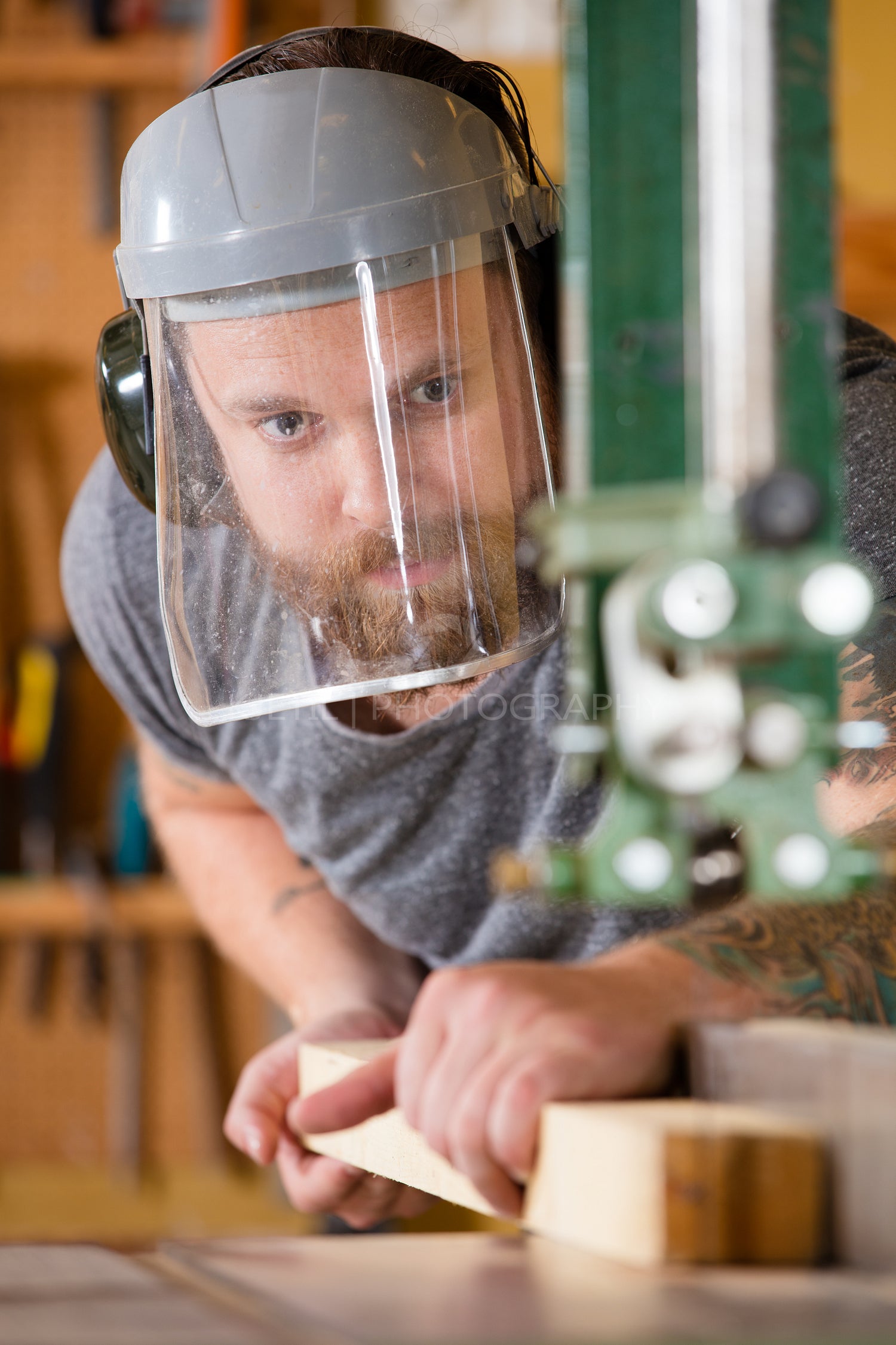 Craftsman with safety mask visor handles band saw in workshop