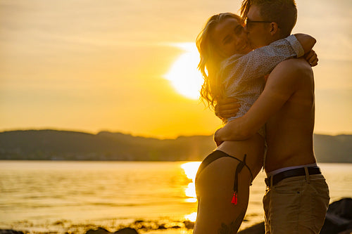 Young Man Kissing Girlfriend Standing At Beach In Beautiful Sunset