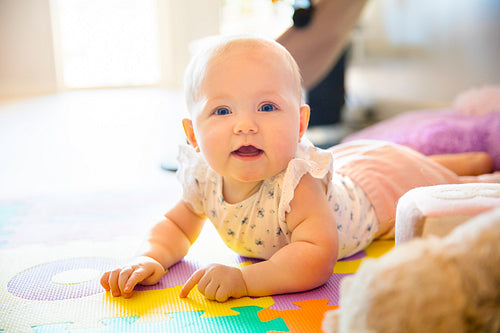 Happy baby girl with blue eyes playing on floor mate