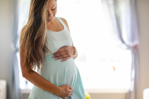 Smiling pregnant woman in dress with her hands at belly