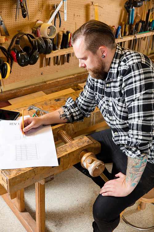 Carpenter plans projects and takes notes on drawing in workshop