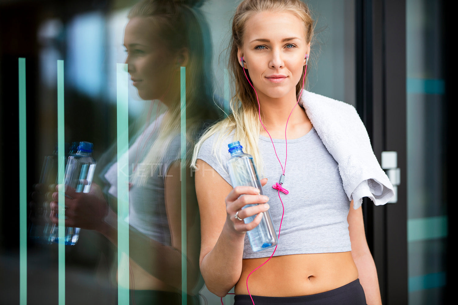 Fit Woman With Water Bottle Leaning Against Glass Wall