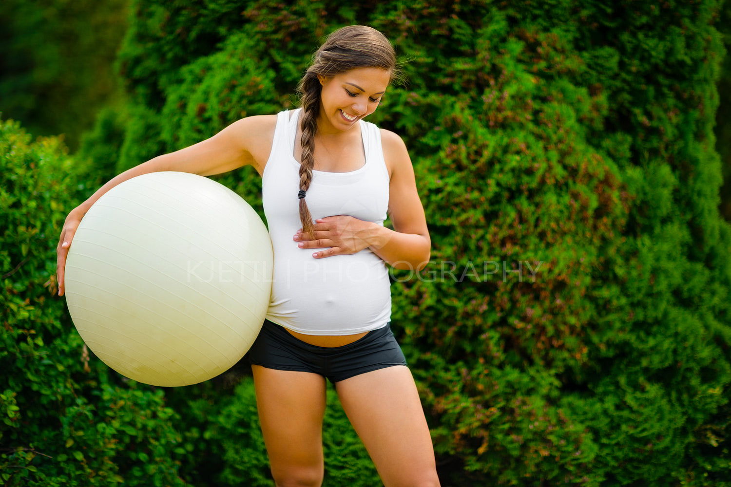 Expectant Mother Touching Stomach While Holding Exercise Ball In Park
