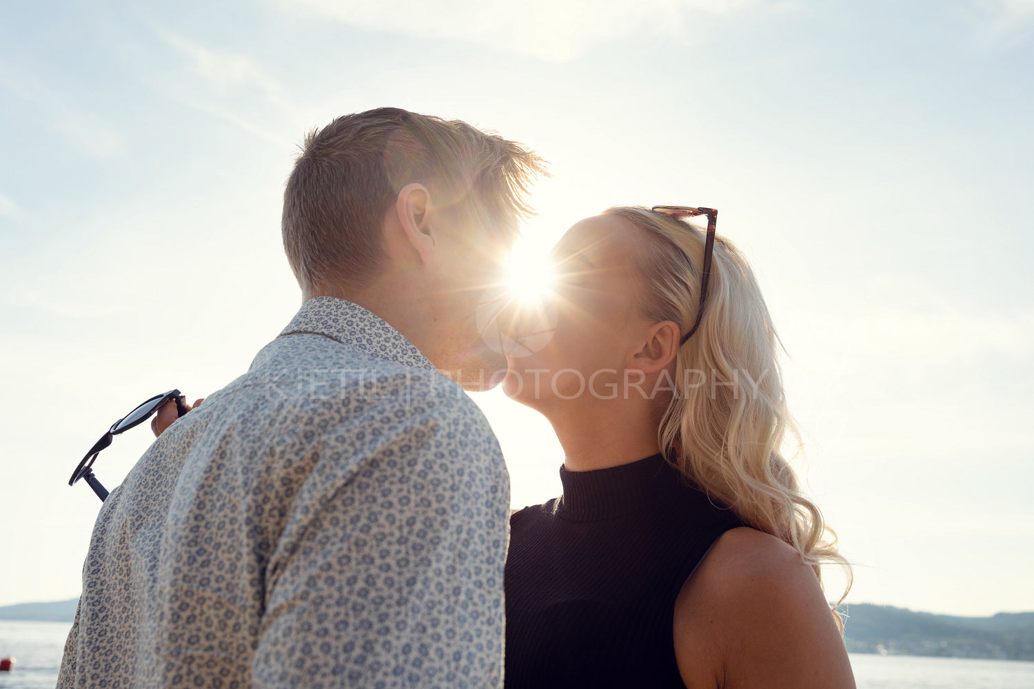 Young Couple Kissing Against Sun At Beach