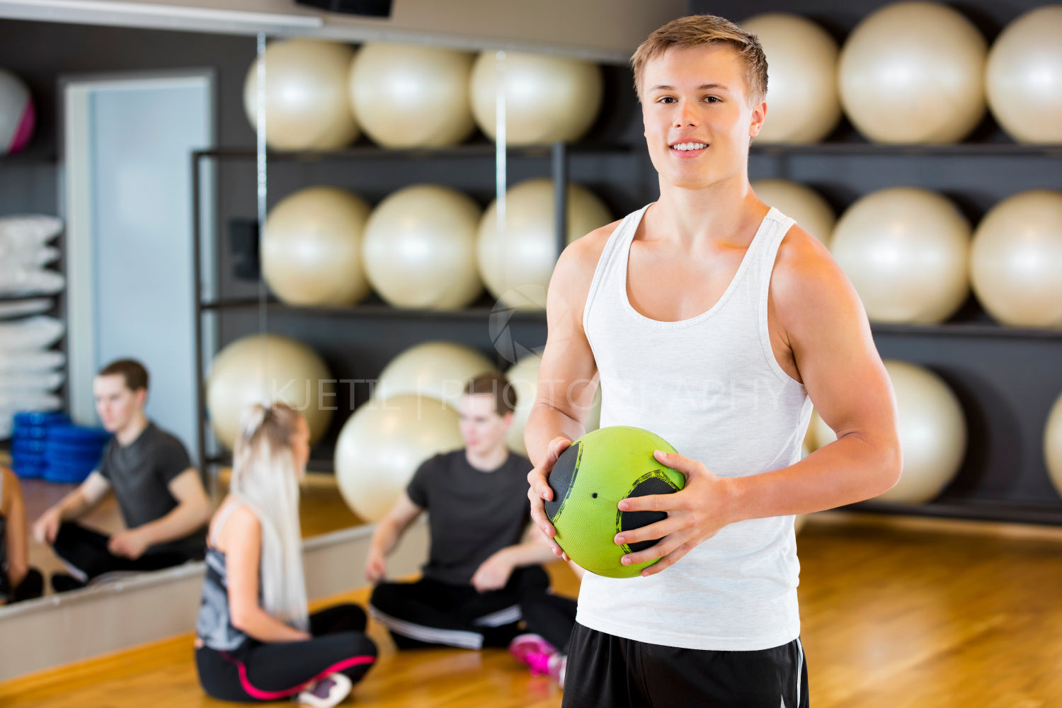 Confident Man Holding Medicine Ball While Friends Resting In Gym