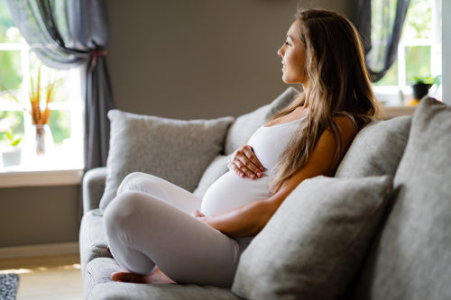 Smiling pregnant woman sitting in sofa touching her belly