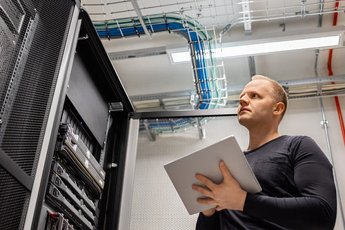 Adult Male Technician Holding Digital Tablet and Analysing Servers in Datacenter
