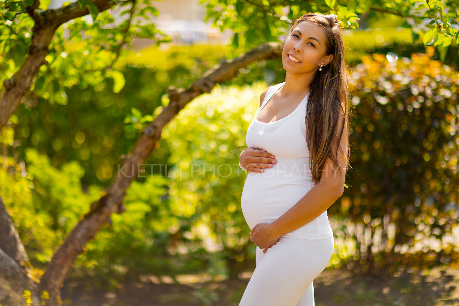 Smiling pregnant woman standing in garden holding on tummy