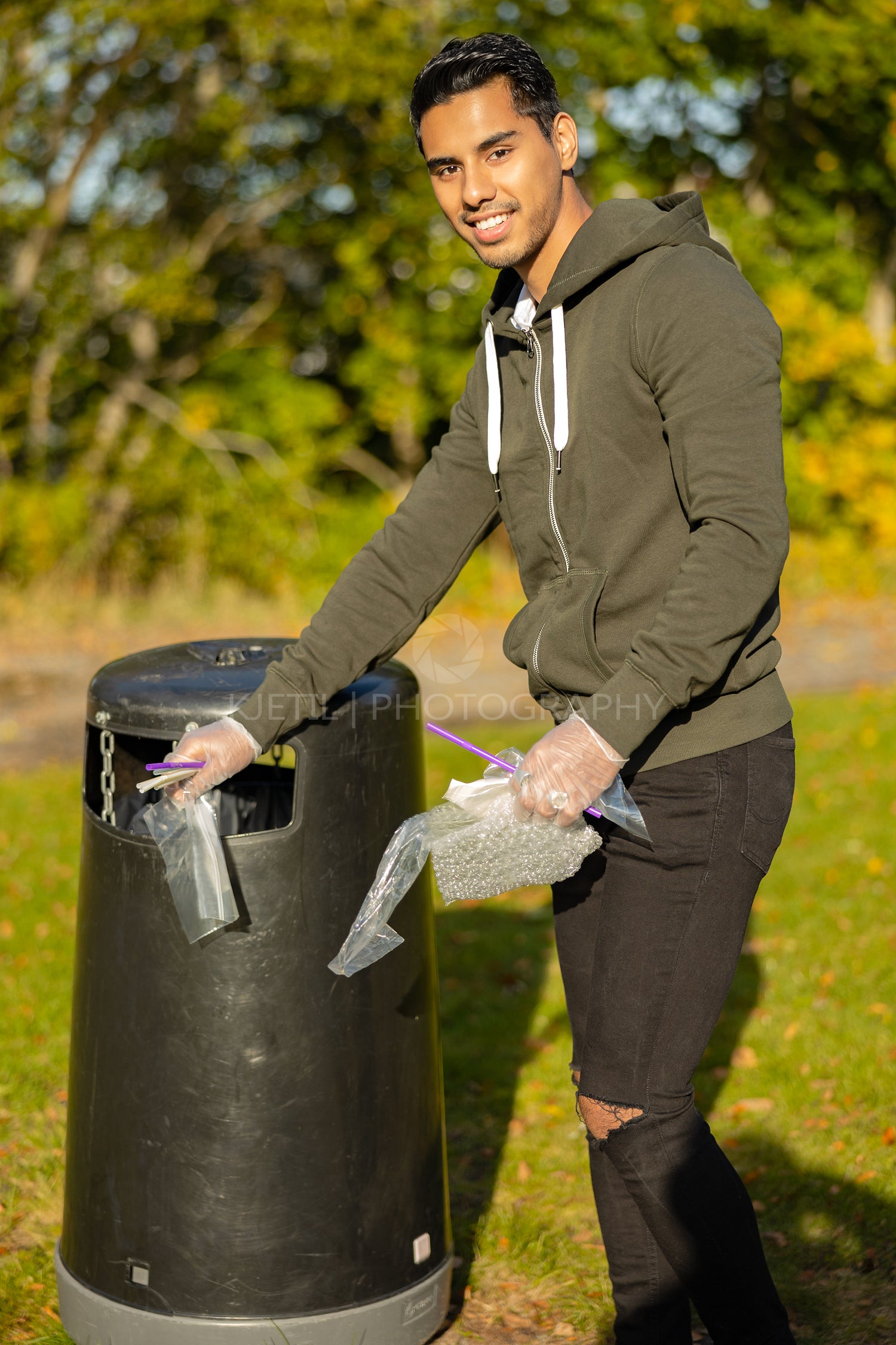 Smiling young man putting plastic in garbage bin at park