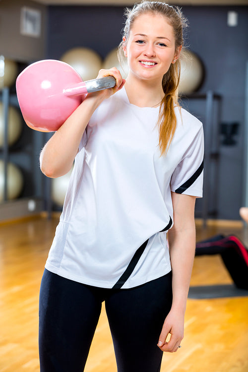 Smiling woman in workout outfit holds kettlebell at fitness gym