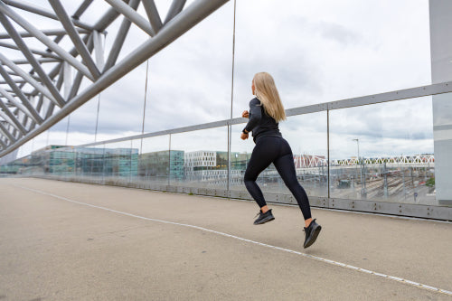 Fast running sporty woman in black workout outfit in modern city environment
