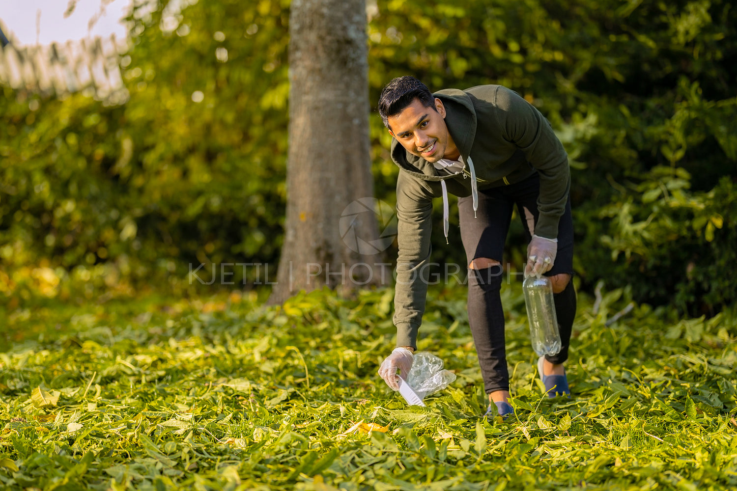 Smiling and committed volunteer cleaning garbage on grass in nature