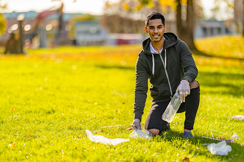 Smiling and committed volunteer cleaning garbage on grass at park