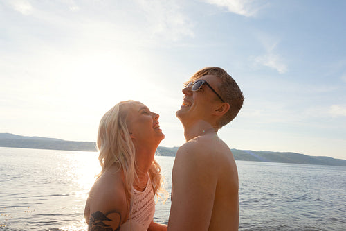 Happy couple in love laughing at the beach against sun