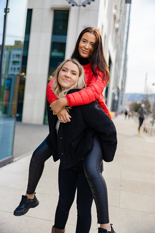 Smiling Female Friends Having Fun and Piggybacking In City Environment