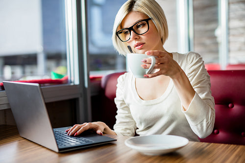 Young Woman Having Coffee While Working On Laptop In Cafe