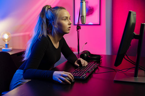 Focused Blonde E-sport Gamer Girl with Headset Playing Online Video Game on PC