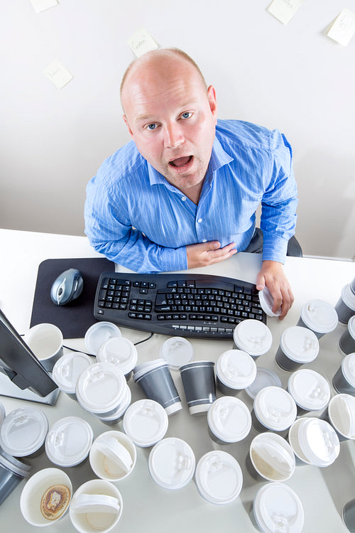 Tired businessman drinks too much coffee at office