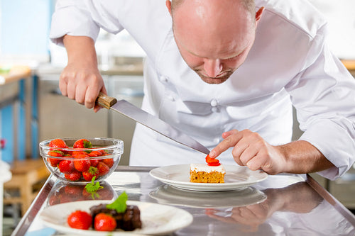 Professional chef decorates dessert cake with strawberry in kitchen