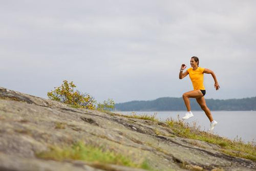 Side view of fitness woman doing high-intensity running on mountainside by the sea